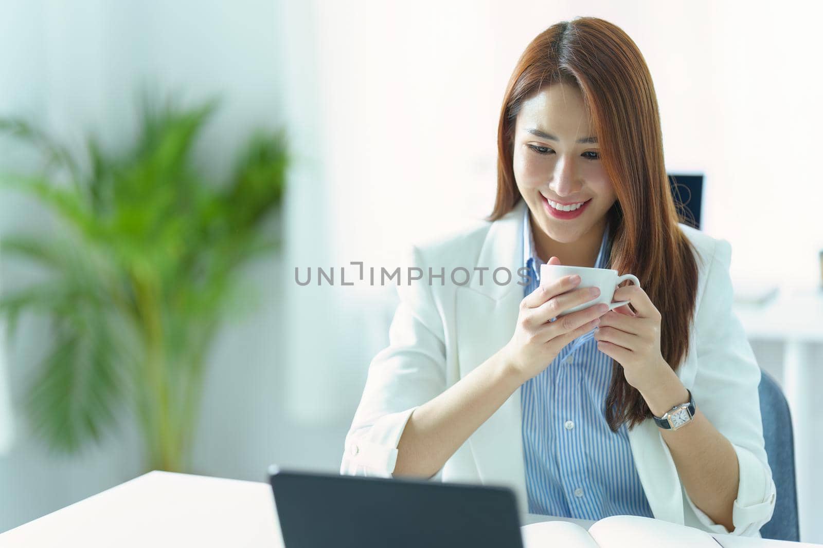 Portrait of an Asian businesswoman or business owner taking a coffee break while working in the office by Manastrong