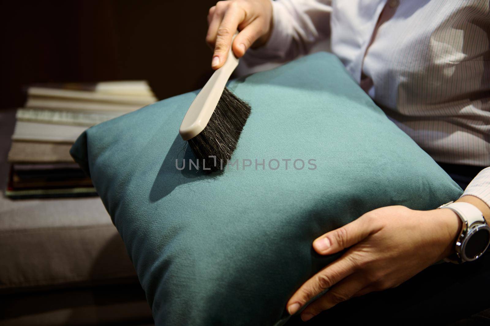 Close-up of the hands of a woman using dustpan cleans a velour pillow from dust. General house cleaning, professional furniture cleaning, cleaning company concept