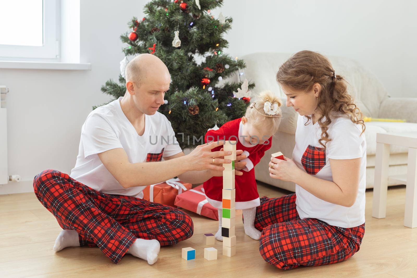 Toddler child with cochlear implant plays with parents under christmas tree - deafness and innovating medical technologies for hearing aid and diversity by Satura86