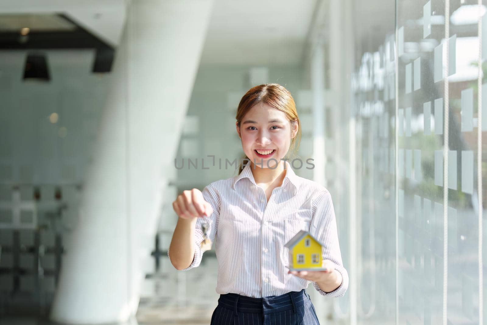 Accountant, real estate agent, Asian business woman handing model house and key to customers along with house interest calculation documents for customers to sign.