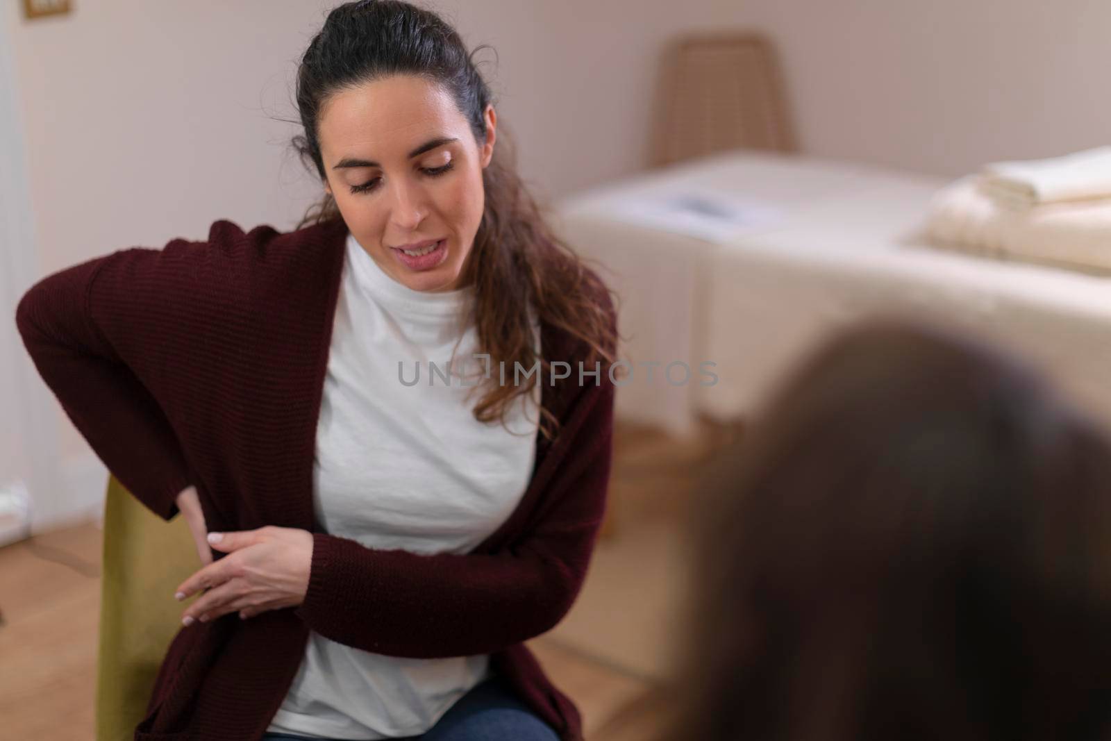 A female patient talks to her therapist in the office, explaining her pain, so that she can offer her a treatment for her health