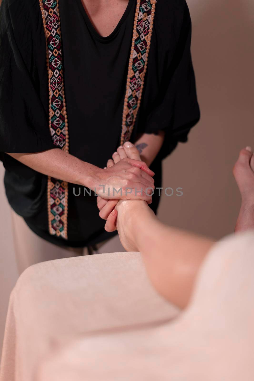 A masseuse massages the feet and legs of her patient, who is lying face up on the table to relieve her health issues and muscle pain