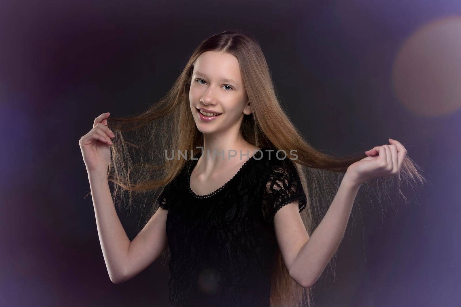 Teenage girl with long hair in a black dress on a background of colored bokeh.