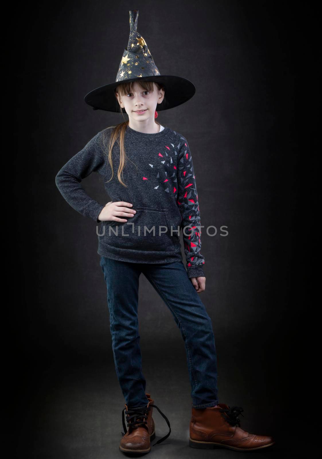 Little girl wearing a witch hat on a dark background.