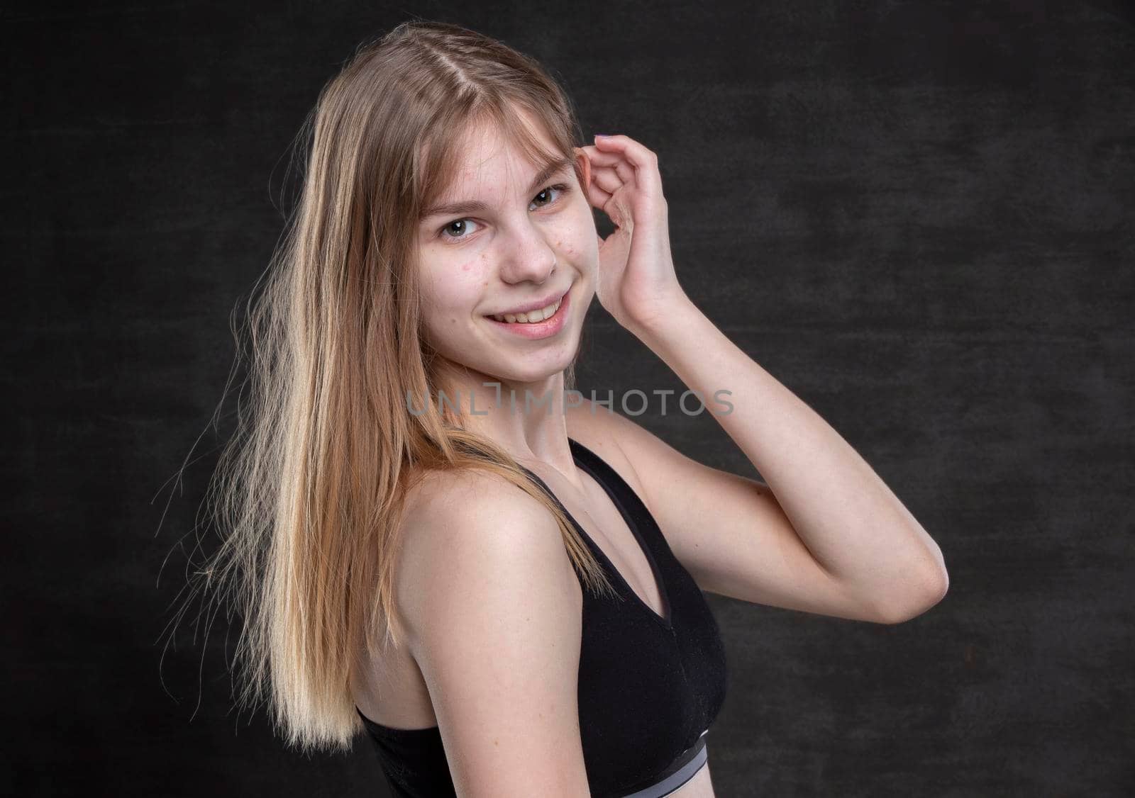 A teenage girl with pimples on her face in a sports shirt on a dark background.