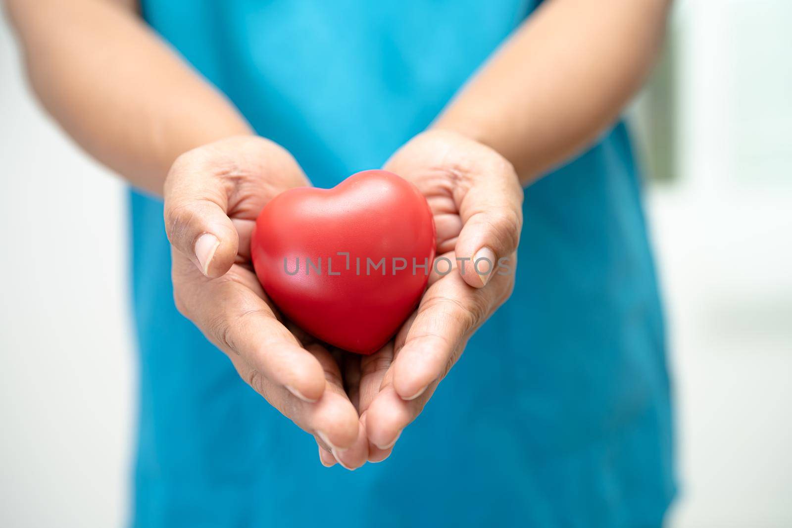 Doctor holding a red heart in hospital ward, healthy strong medical concept.