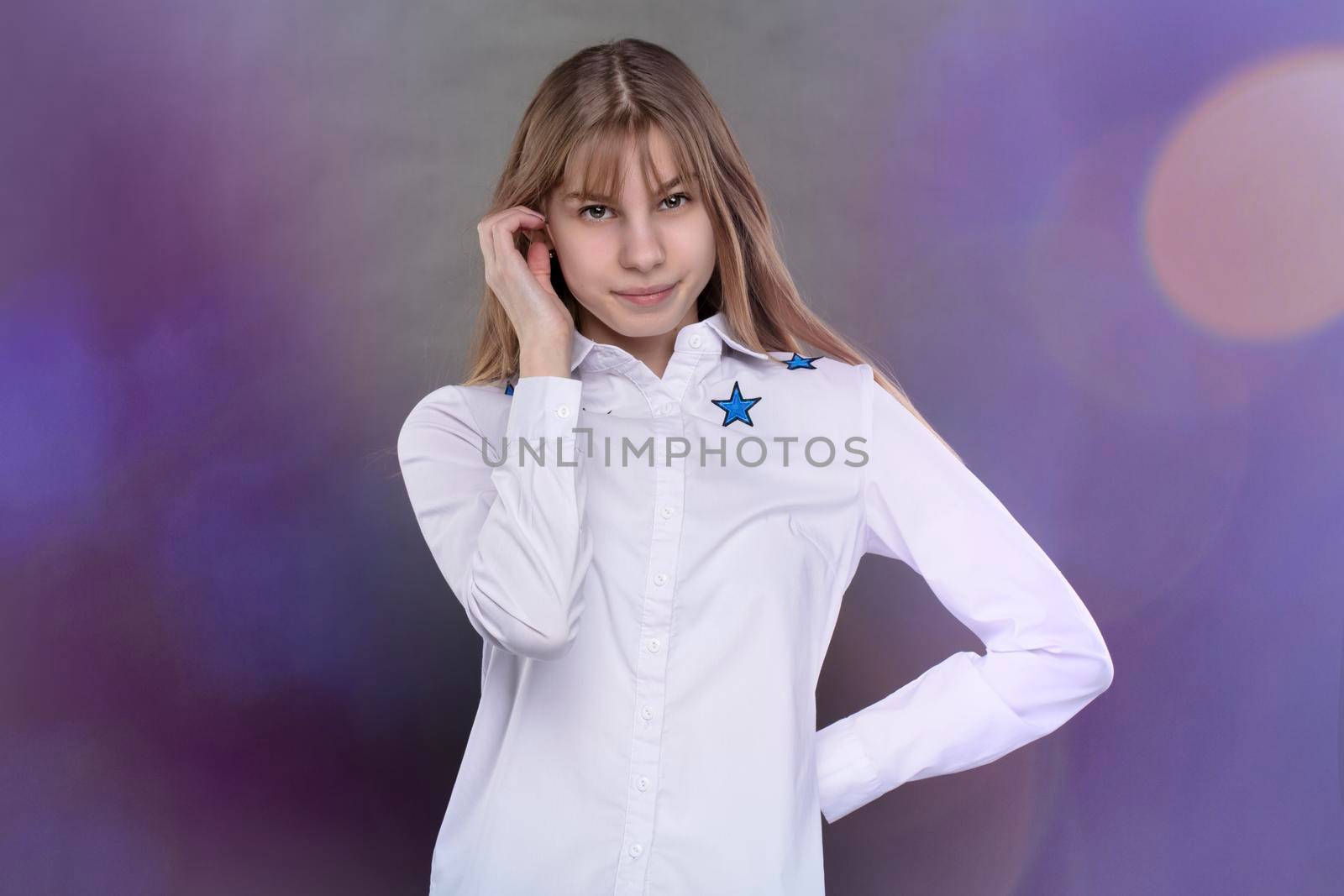 Happy teenage girl in a white shirt is shot against a gray background.