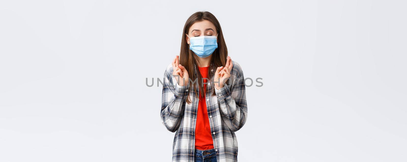 Coronavirus outbreak, leisure on quarantine, social distancing and emotions concept. Hopeful cute young woman in medical mask praying, close eyes and cross fingers good luck, making wish.