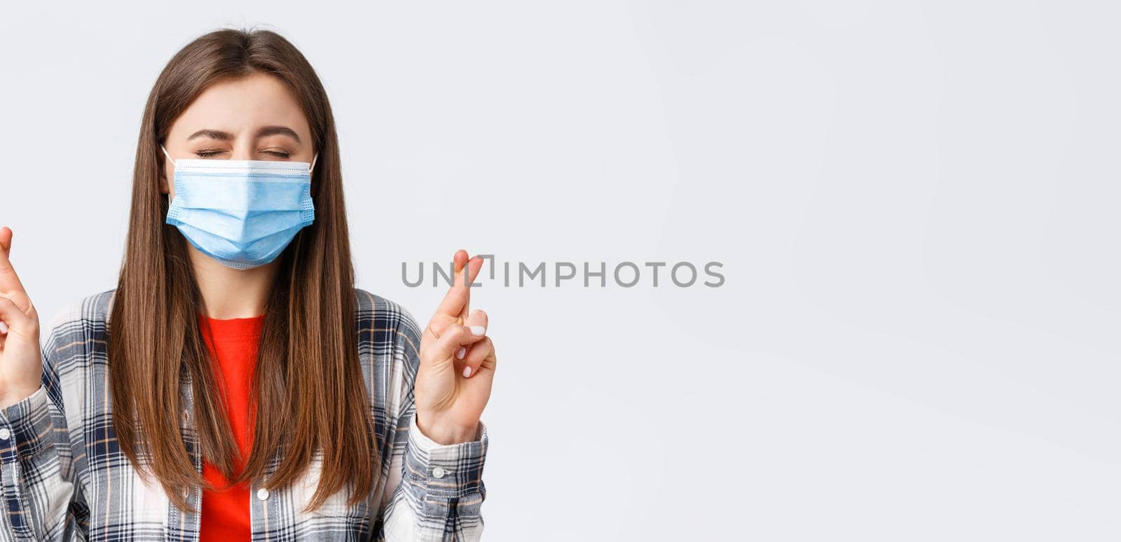 Coronavirus outbreak, leisure on quarantine, social distancing and emotions concept. Close-up of hopeful, dreamy young girl making wish, close eyes and cross fingers good luck.