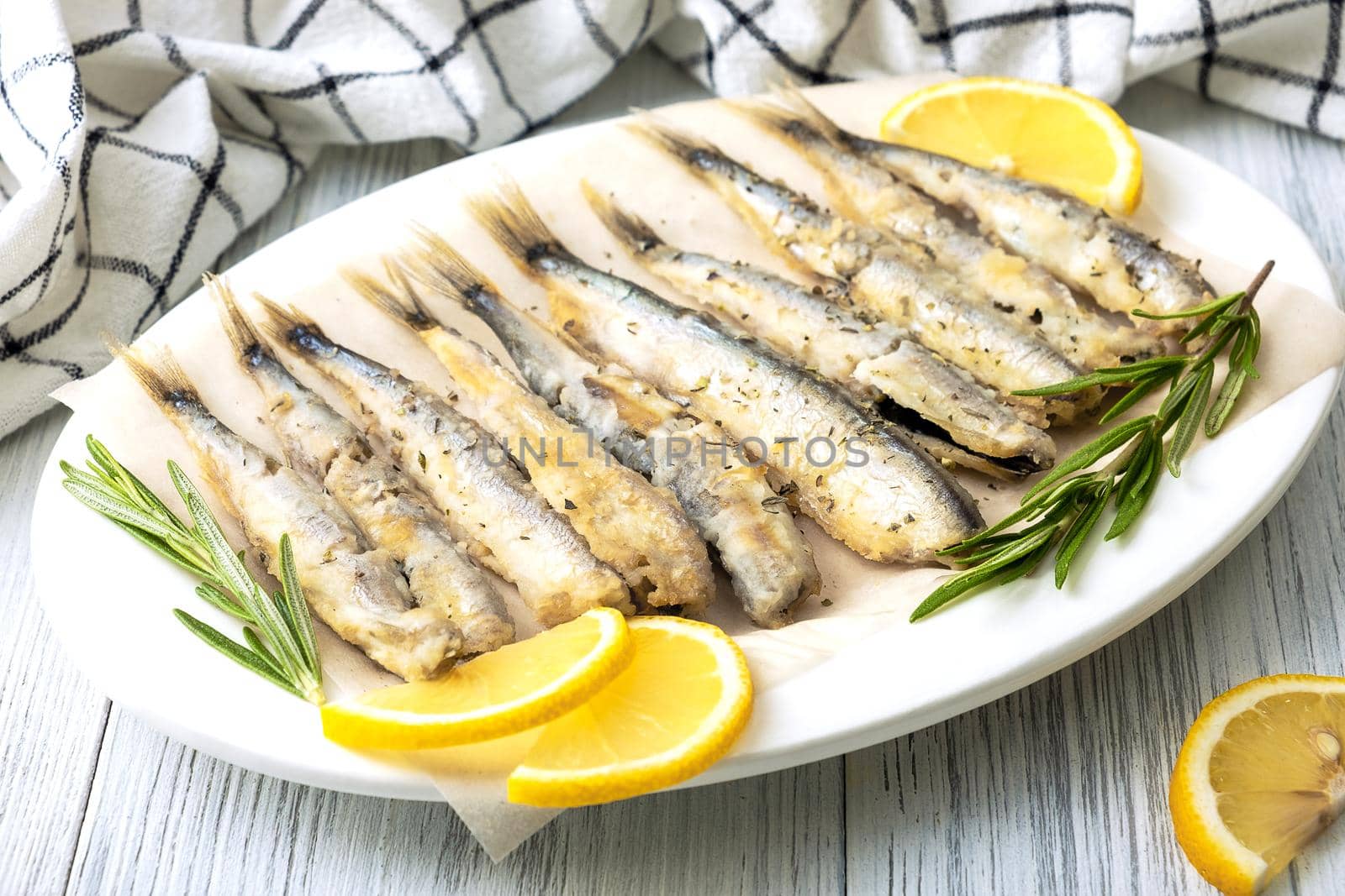 Close-up of fried capelin on a white porcelain dish with lemon, rosemary and spices. Healthy food concept. Selective focus.