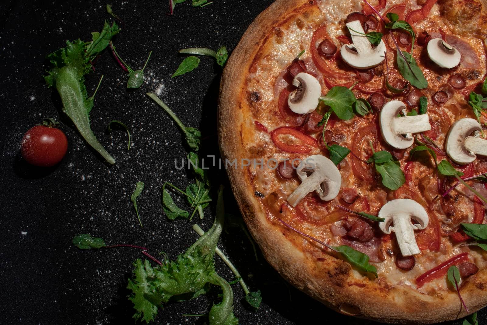 Top view of tasty appetizing classic italian traditional pizza with cheese, olives, basil and fresh vegetables on dark black table.