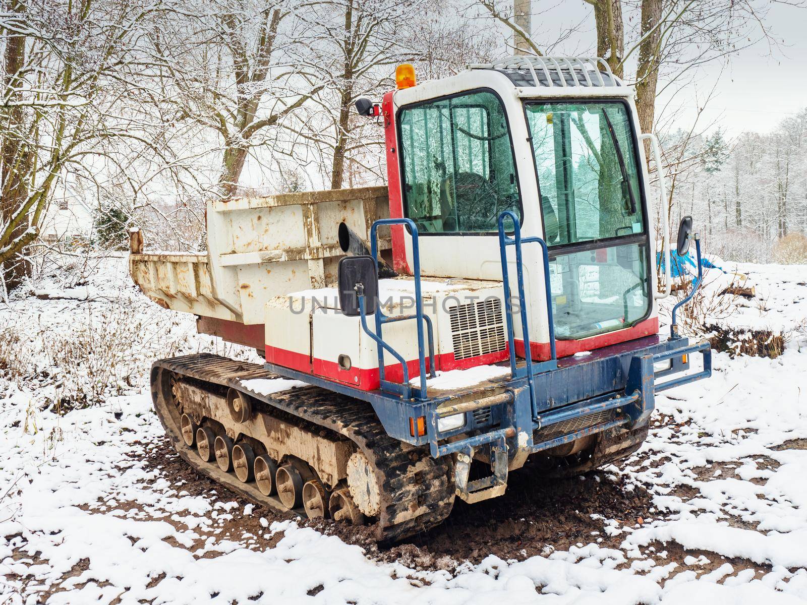 Small Dumper Tracked Truck with Muddy Chassis. The transporter waiting in the snowy forest