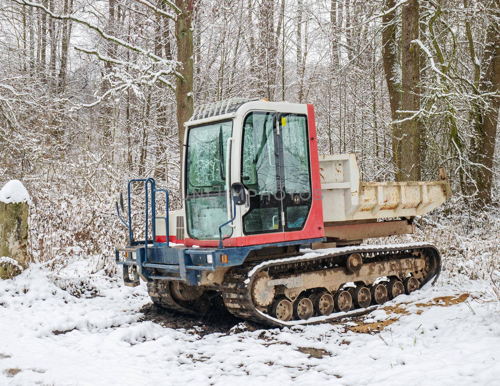 Small Dumper Tracked Truck with Muddy Chassis. The transporter waiting in the snowy forest
