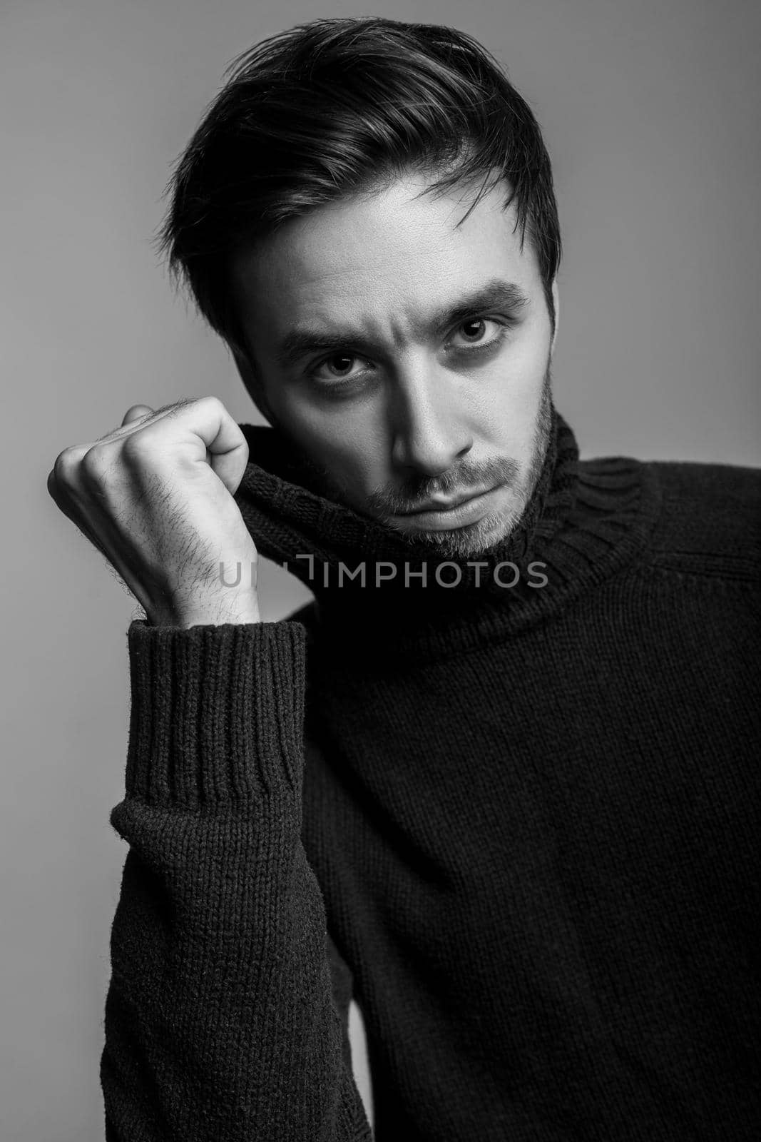 Portrait of sexy handsome man with stylish hairdo wearing warm sweater, pulling sweater collar and looking seductive, flirting at camera, male fashion, vogue concept. black and white, indoor isolated