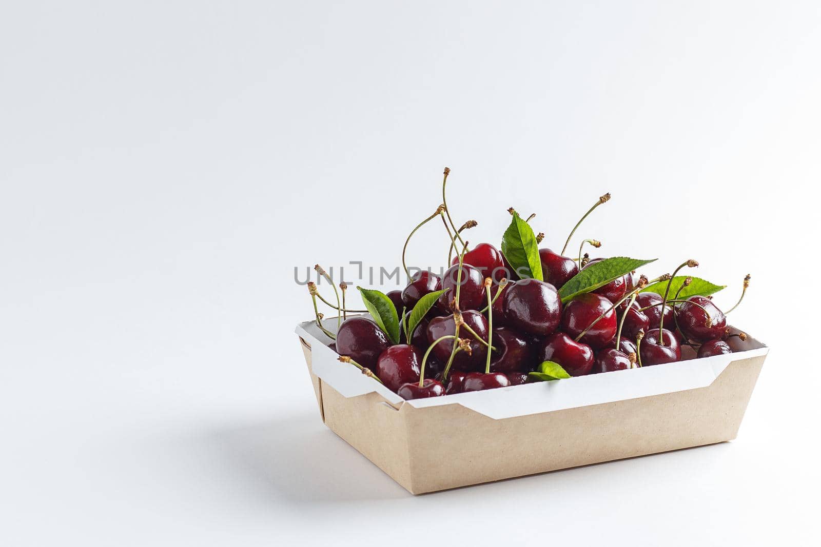 Fresh, ripe cherries in a cardboard box on a white background. Copy space by lara29
