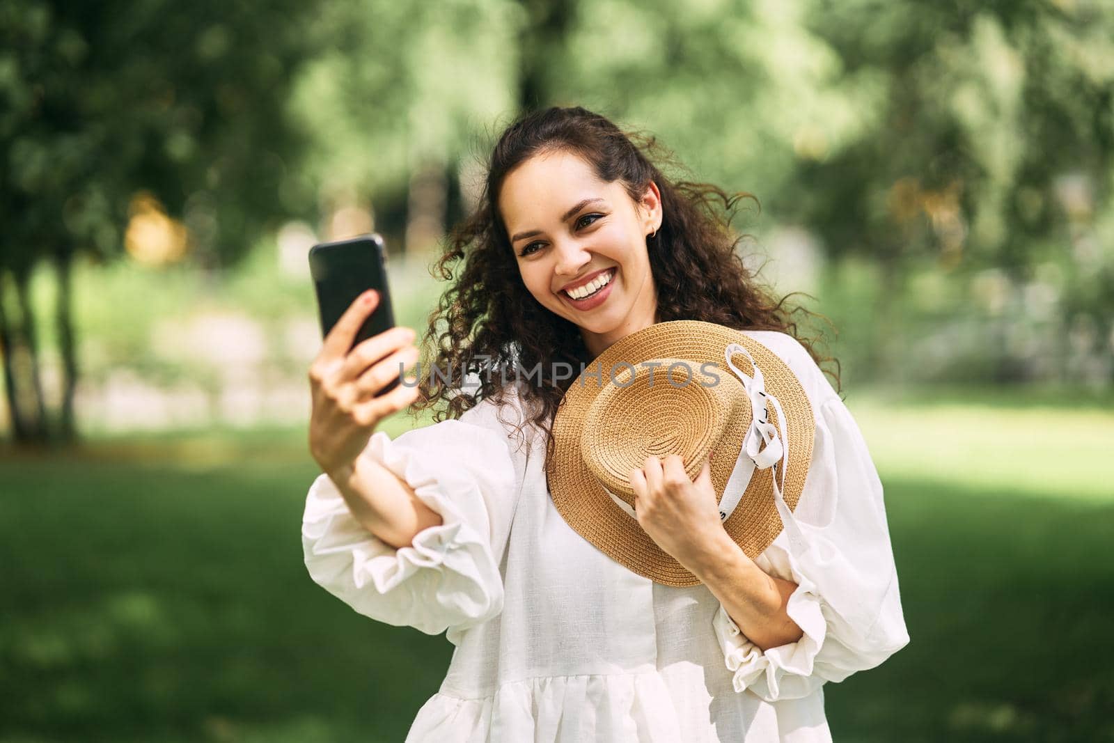 Young beautiful girl in a hat makes a selfie on her phone in the park by driver-s