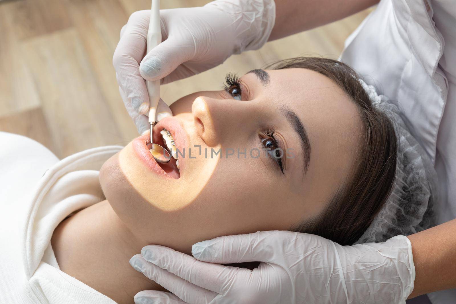 Young woman having dental check up in dental clinic. Dentist examining a patient teeth with dental mirror by Mariakray