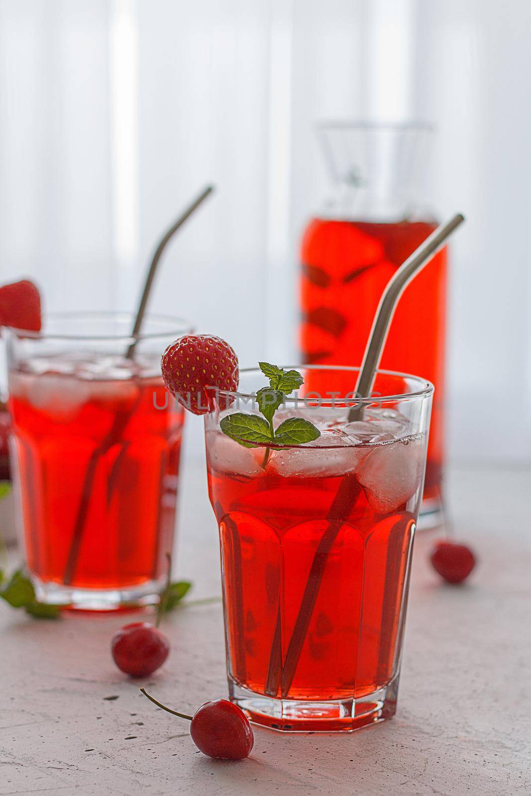 Red refreshing drink with mint on a gray background. Colorful summer non-alcoholic refreshing drink with ice made from berries. Vertical photo