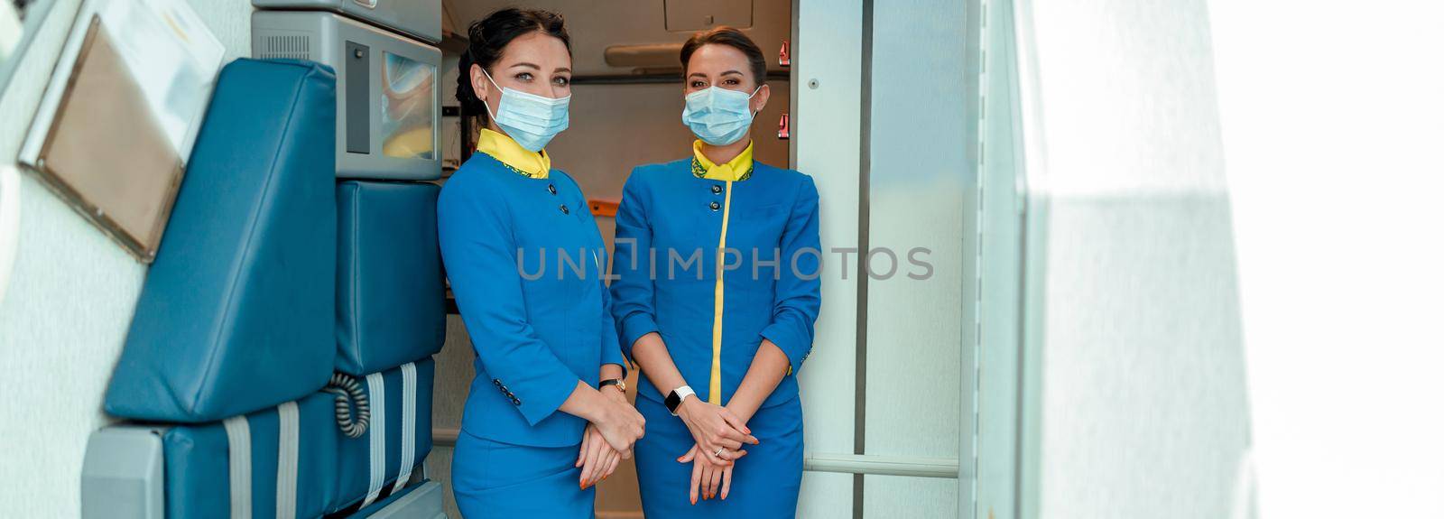 Flight attendants in medical masks standing in airplane cabin by Yaroslav_astakhov