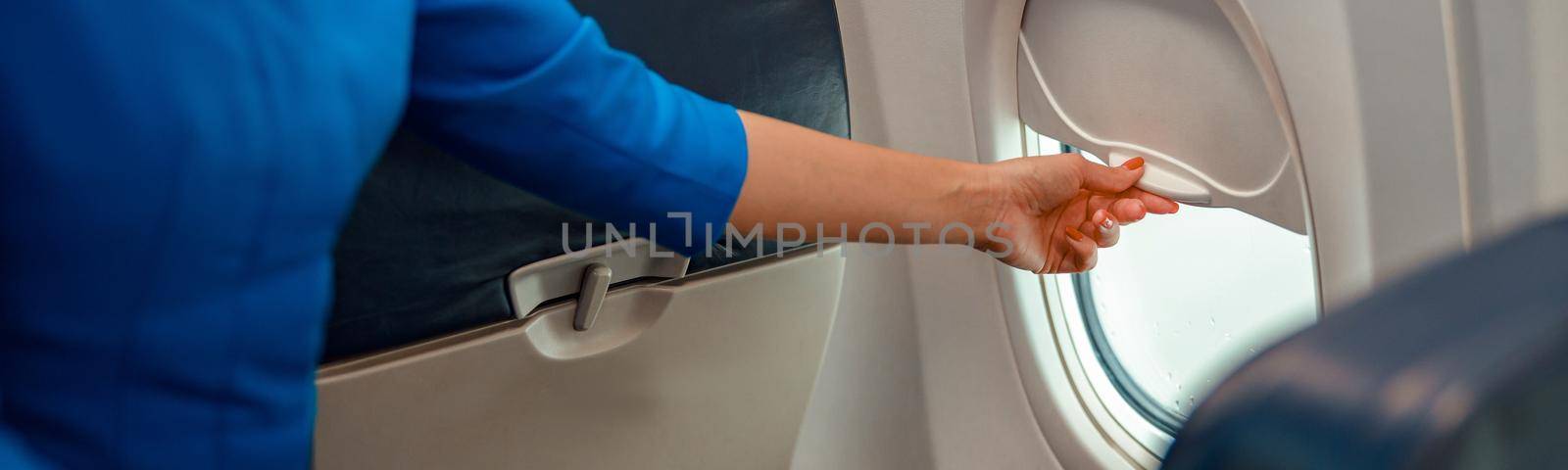Woman flight attendant closing window in airplane by Yaroslav_astakhov