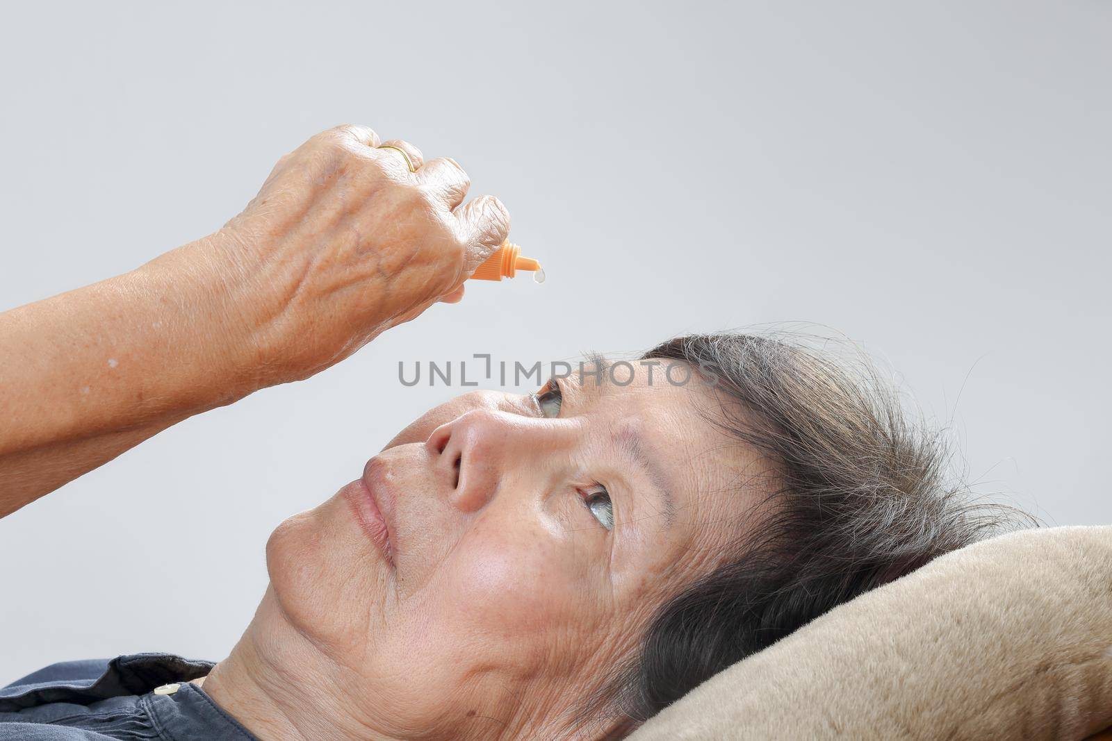 elderly woman applying eye drops on bed by toa55