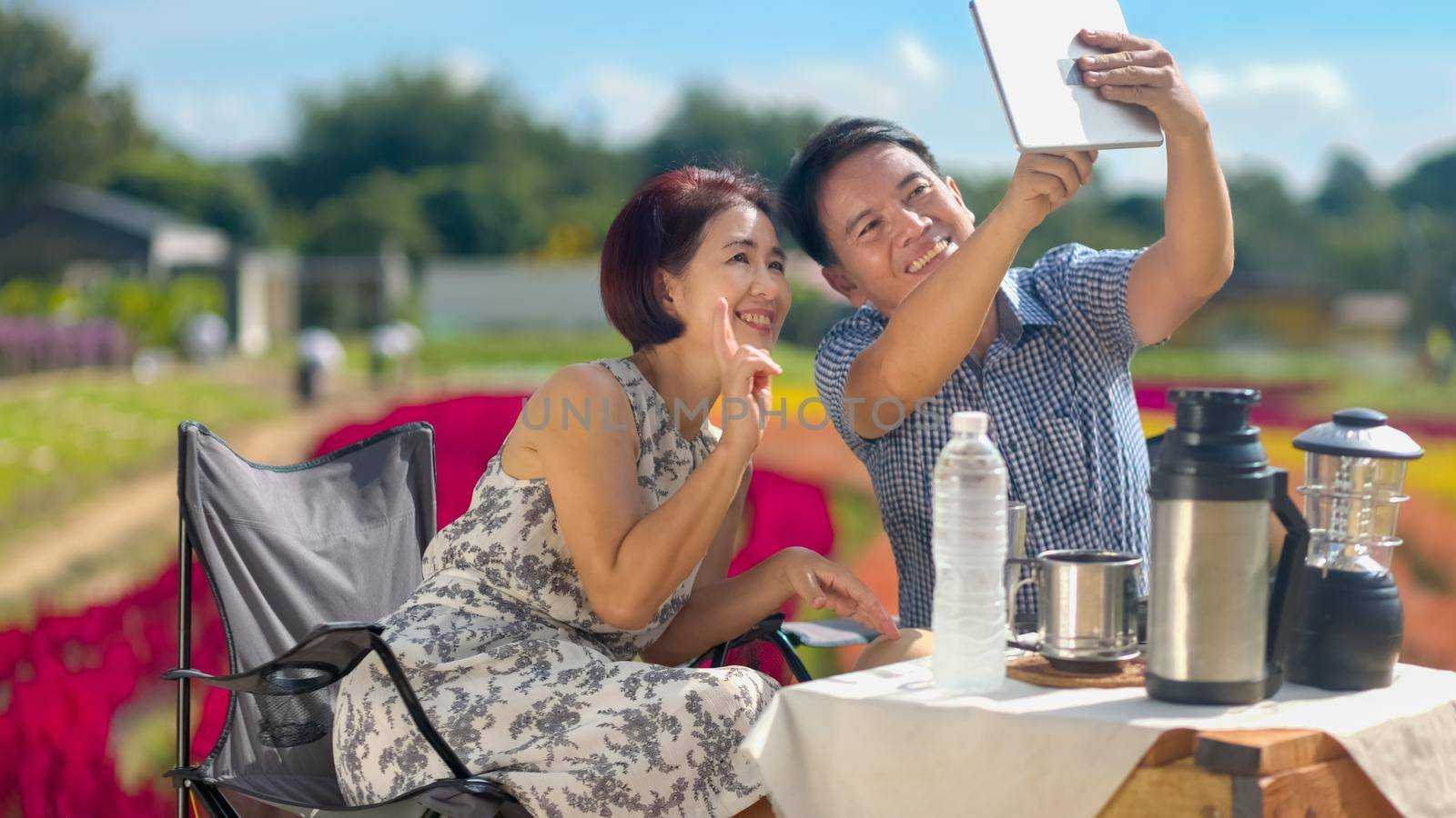 Happy middle aged couple selfie together while relaxed sitting in flower garden. by toa55