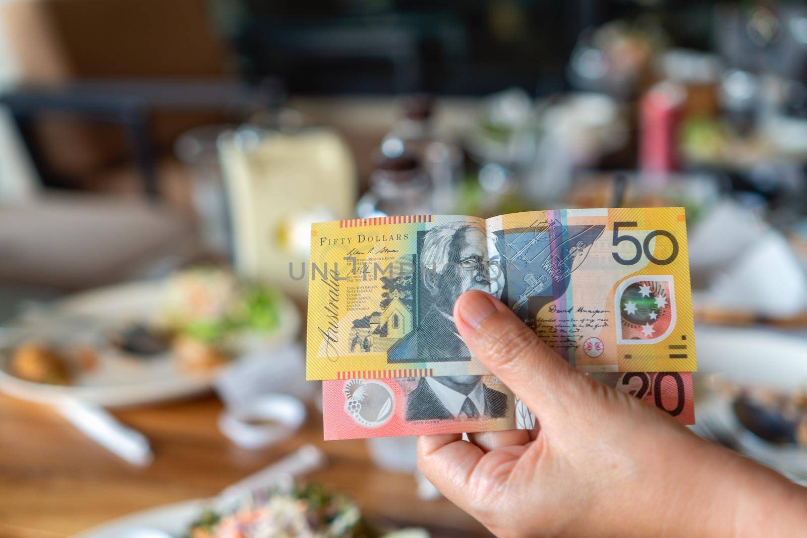 Woman's hand holding Australian notes to make a payment in restaurant. by toa55