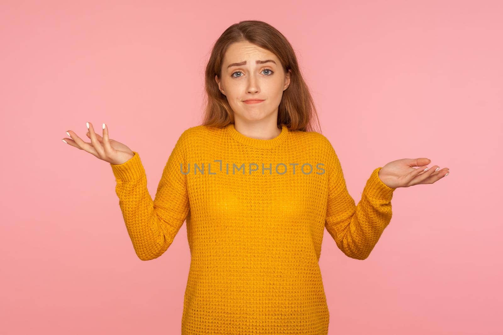 No idea, I don't know. Portrait of uncertain confused ginger girl in sweater expressing doubts and bewilderment, looking at camera with question so what, who cares. indoor studio shot pink background