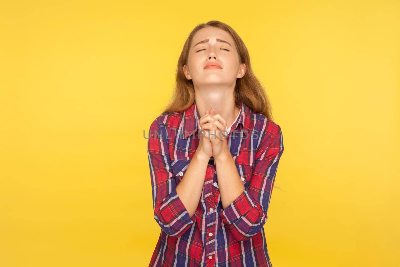 Please I'm begging. Portrait of despaired ginger girl in shirt keeping arms in prayer gesture and holding up head, appealing to god with imploring expression. studio shot isolated on yellow background