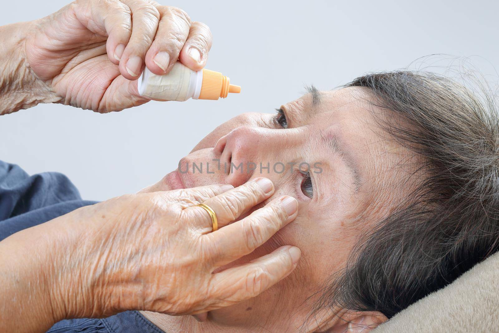 elderly woman applying eye drops on bed