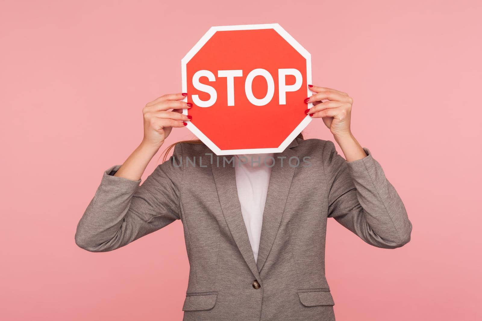 Portrait of unknown business person in suit jacket covering face with Stop symbol, anonymous woman holding red traffic sign stop, warning of danger, restriction and limits. indoor studio shot isolated