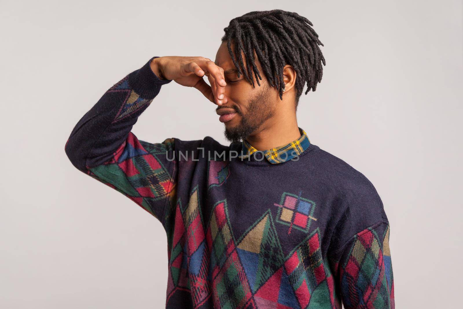 Profile portrait bearded african guy with dreadlocks pinching his nose with fingers feeling unpleasant disgusting odor, spoiled food. Indoor studio shot isolated on gray background