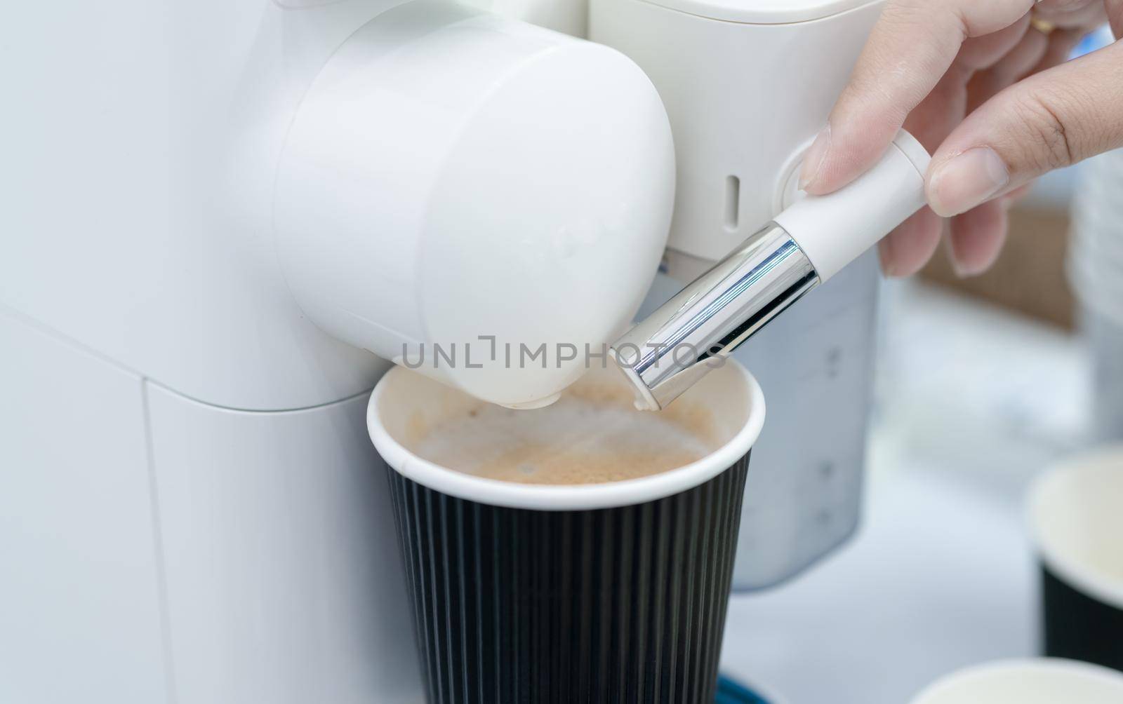 Woman making a cup of hot coffee with capsule coffee machine. Woman hand holding frothed milk dispenser of capsule coffee machine on table. Espresso coffee maker. Morning drink. Modern home equipment.