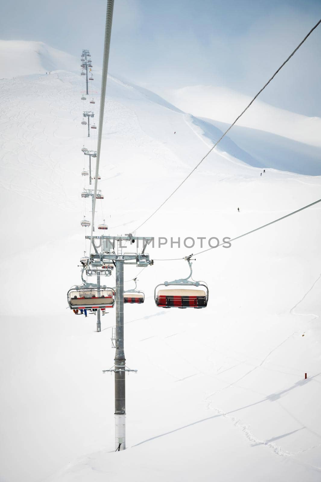 An open-air lift that goes to the top of the mountain for downhill skiing. Sunny day surrounded by snowy fields. Ski resort slope in good weather.