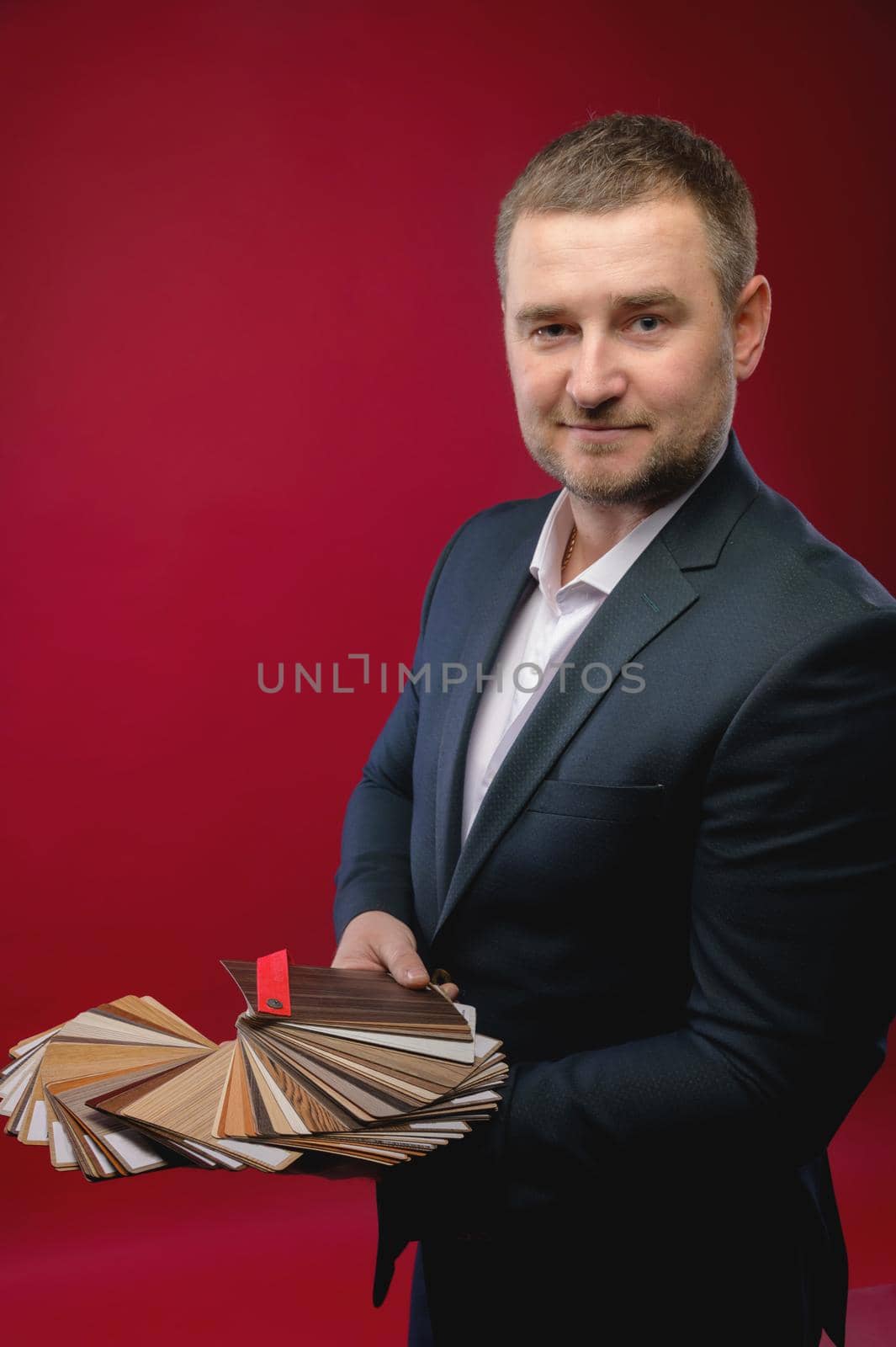 Portrait of a handsome man in an elegant suit Offers surface probes for kitchen furniture on a red background. Studio shot looking thoughtfully into the camera.