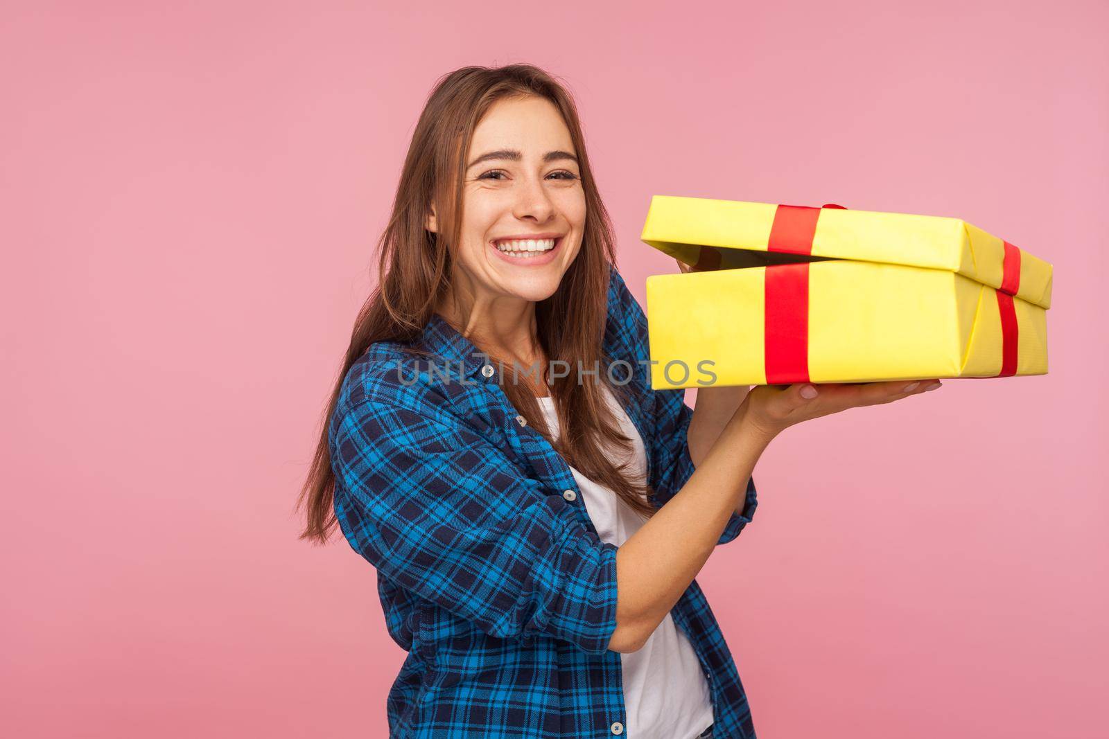Nice holiday present, bonus. Portrait of happy beautiful girl in checkered shirt holding unwrapped box and looking at camera with toothy smile, excited about birthday gift. indoor studio shot isolated