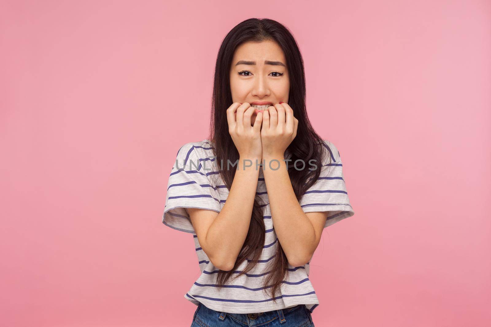 Troubles and worries. Portrait of nervous girl with long brunette hair biting nails and looking frightened, terrified about problems, suffering phobia, anxiety disorder. indoor studio shot isolated