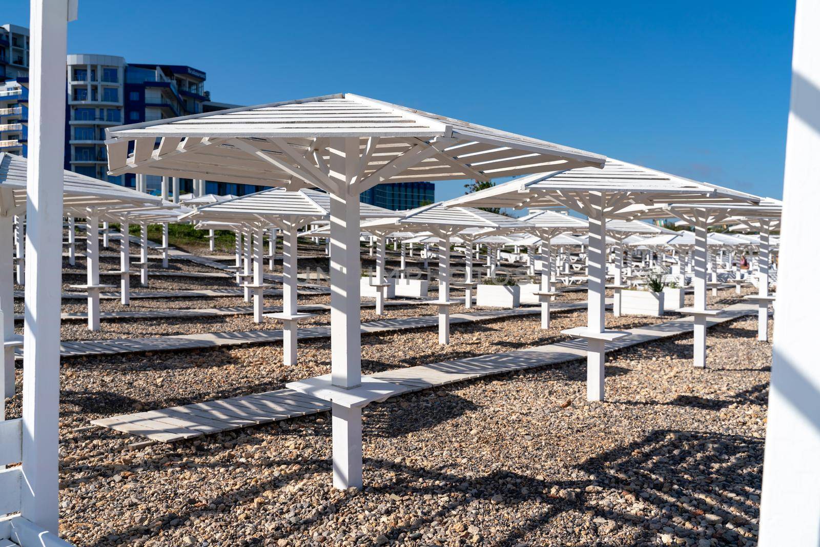 Rows of wooden umbrellas from the sun on the seashore in the morning. Wooden paths on the sand between umbrellas. Beach holiday at the resort