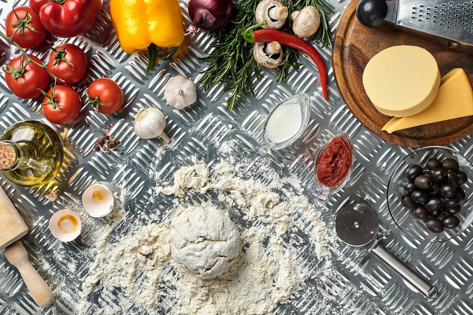 Ingredients and dough for making pizzas with an overhead view on freshly mixed mounds of pastry, a jar of olive oil and pot of tomato sauce, overhead view on metal background. Top view. Flat lay. Still life