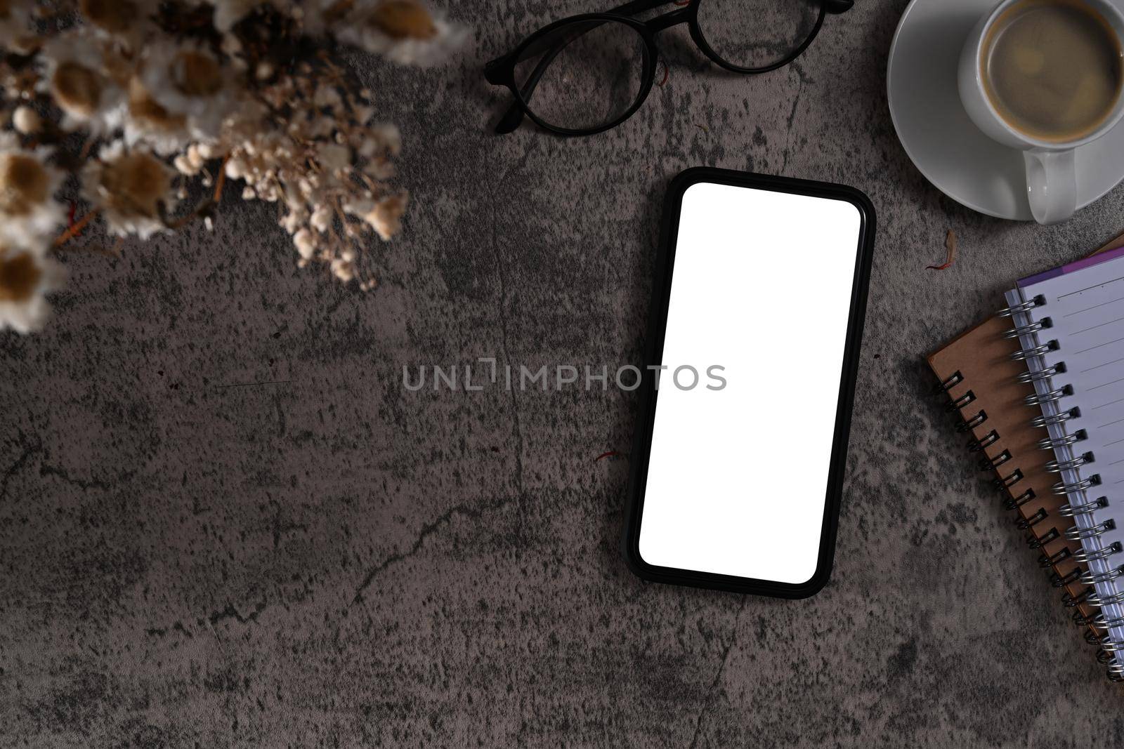 Top view mockup mobile phone with blank screen, eyeglasses an coffee cup on ark stone background by prathanchorruangsak