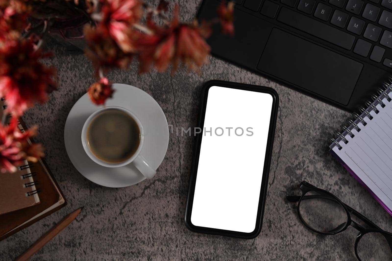 Smart phone with white display, coffee cup, eyeglasses and notebook on stone background by prathanchorruangsak