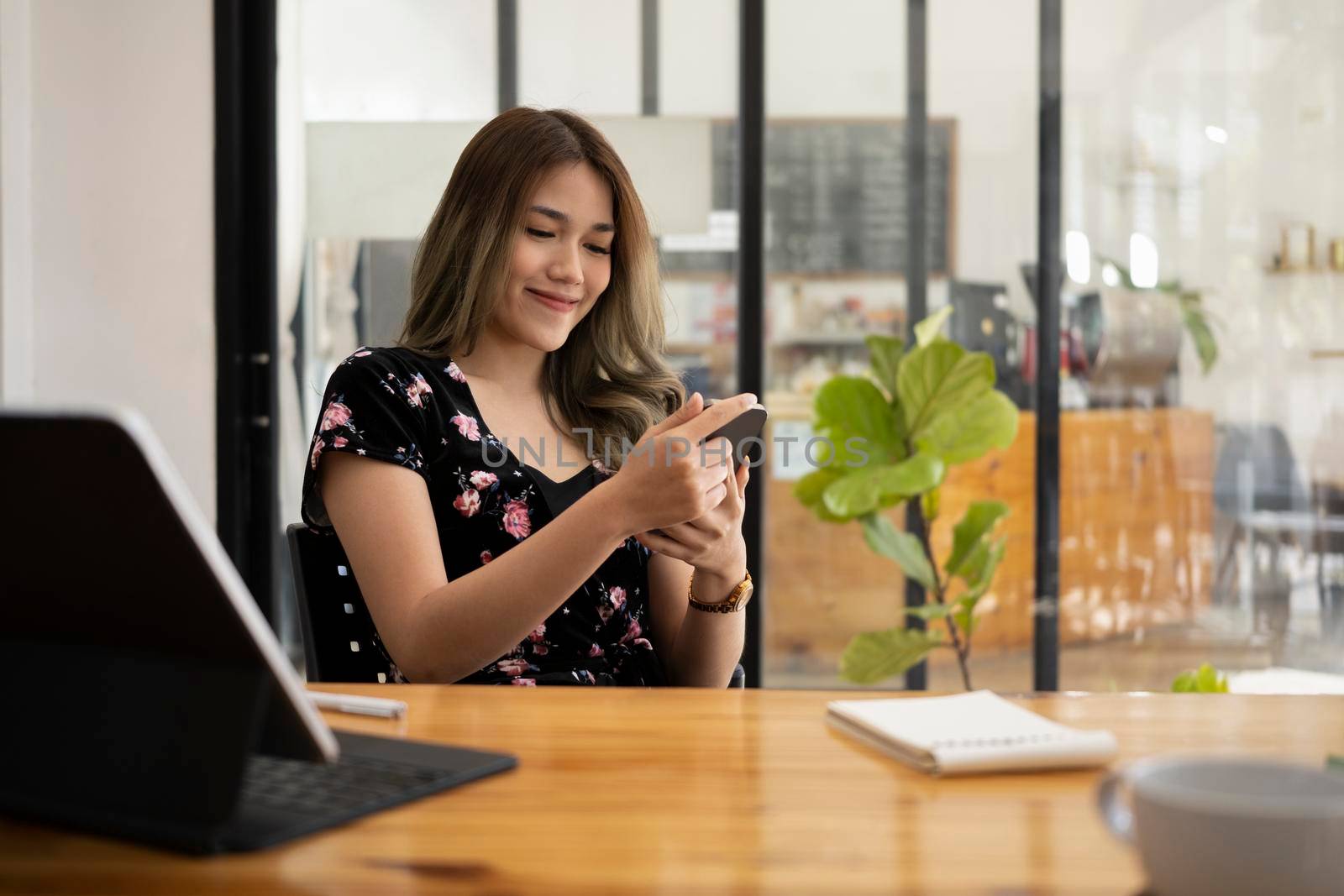 Happy young woman sitting in modern coffee shop and checking social media on her mobile phone.