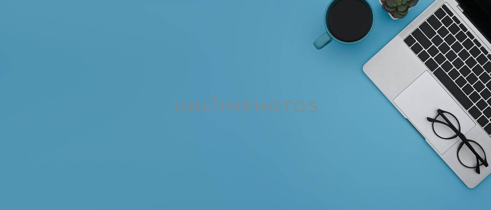 Top view laptop computer, coffee cup and glasses on blue background with copy pace. by prathanchorruangsak