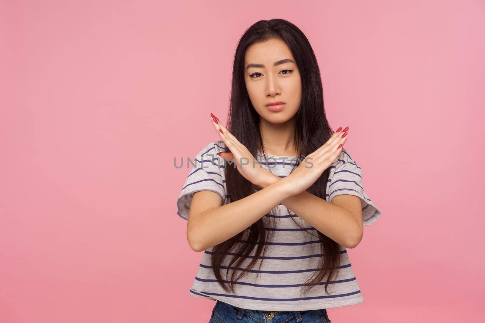 No way, stop doing, Portrait of serious girl with brunette hair in striped t-shirt making x sign with crossed hands, gesturing stop, warning of danger. indoor studio shot isolated on pink background