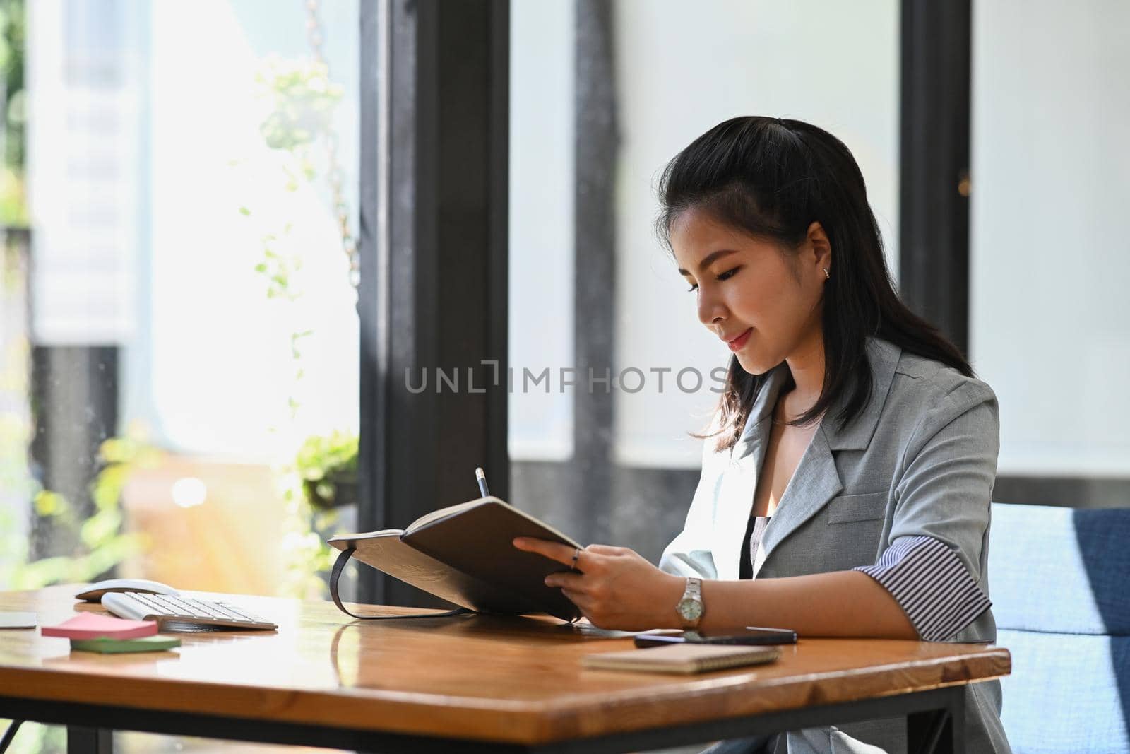 Concentrated businesswoman sitting at her office desk and making note on notebook.