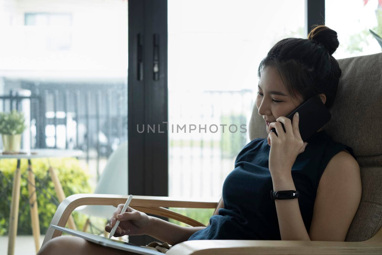 Young woman using digital table and talking on mobile phone in bright living room. by prathanchorruangsak