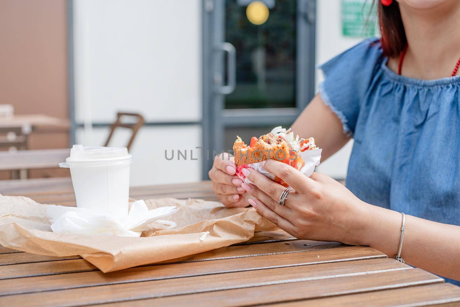 closeup of woman hands holding hamburger, woman eating fast food at street cafe by Desperada