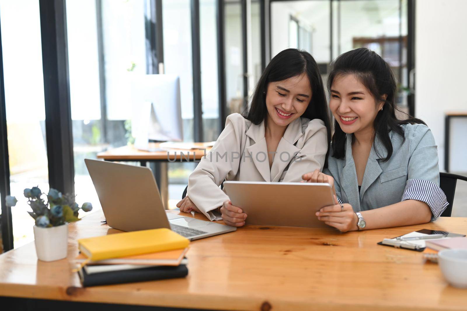 Two cheerful female business colleagues sharing information and discussing work together. by prathanchorruangsak