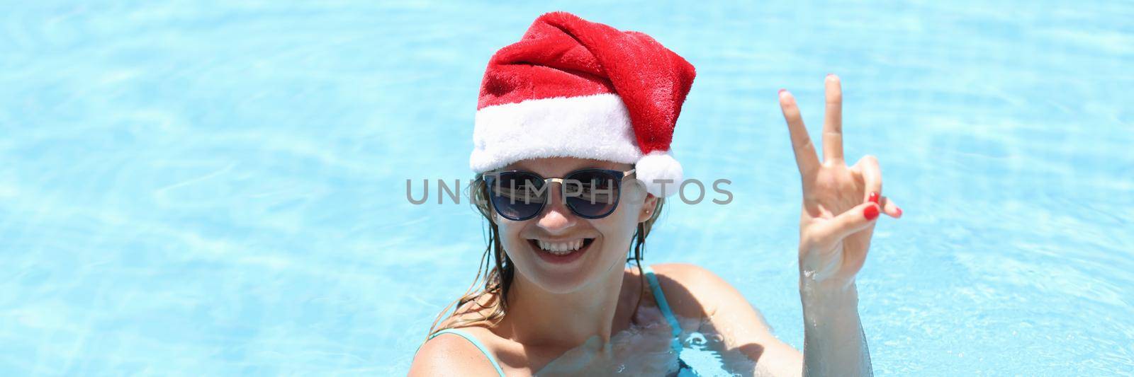 Young smiling woman in santa claus hat in pool by kuprevich
