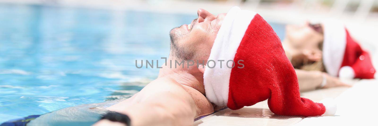 Young people in santa claus hats lie relaxed in pool. Tourism vacation for New Year holidays concept